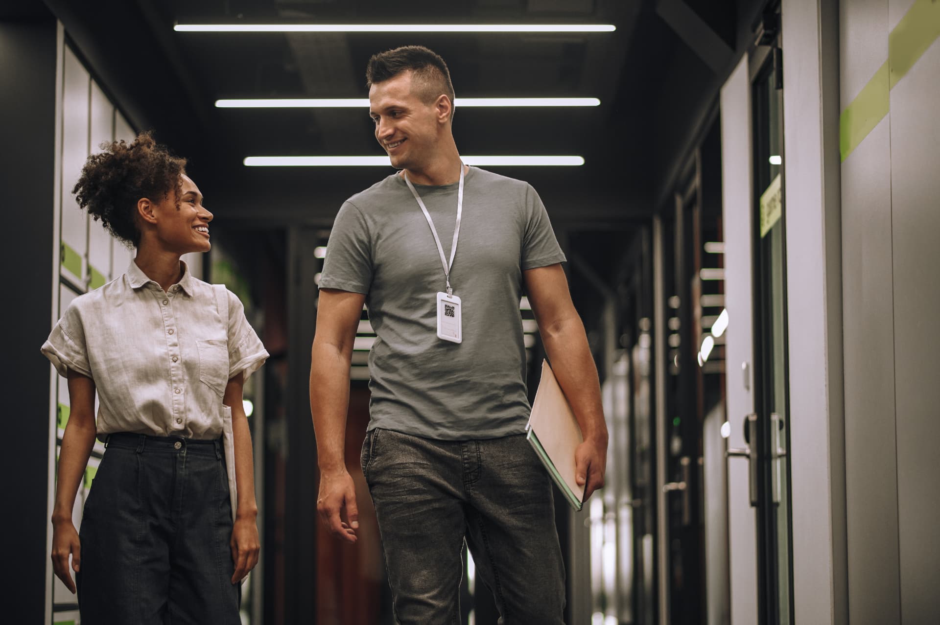 Dois colegas de trabalho conversando e sorrindo em corredor de empresa