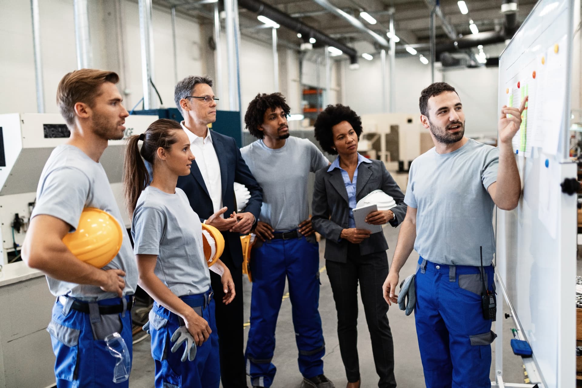 Trabalhadores e líderes reunidos em ambiente industrial ao redor de quadro branco
